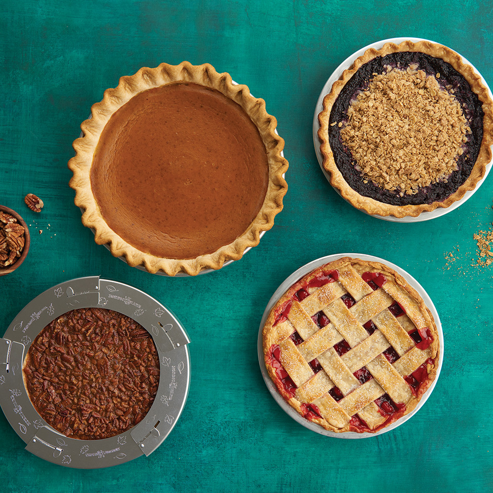 Four baked pies in Nordic Ware aluminum pie pans with pie shield, showing different fillings and crust styles