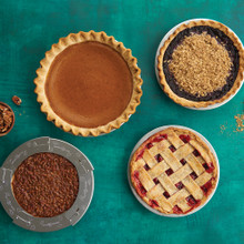Four baked pies in Nordic Ware aluminum pie pans with pie shield, showing different fillings and crust styles