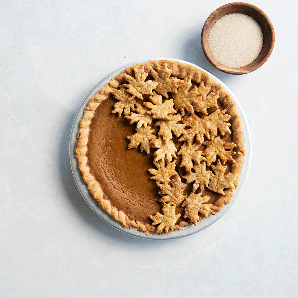 Baked pumpkin pie in Nordic Ware aluminum pie pan with decorative pastry leaves being placed on top