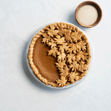 Baked pumpkin pie in Nordic Ware aluminum pie pan with decorative pastry leaves being placed on top