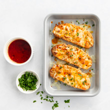 Nordic Ware aluminum eighth sheet pan with golden cheesy garlic bread, small bowl of dipping sauce and garlic cloves