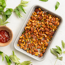 Nordic Ware aluminum eighth sheet pan with mixed nuts, small bowl of spices, and green leaves arranged overhead