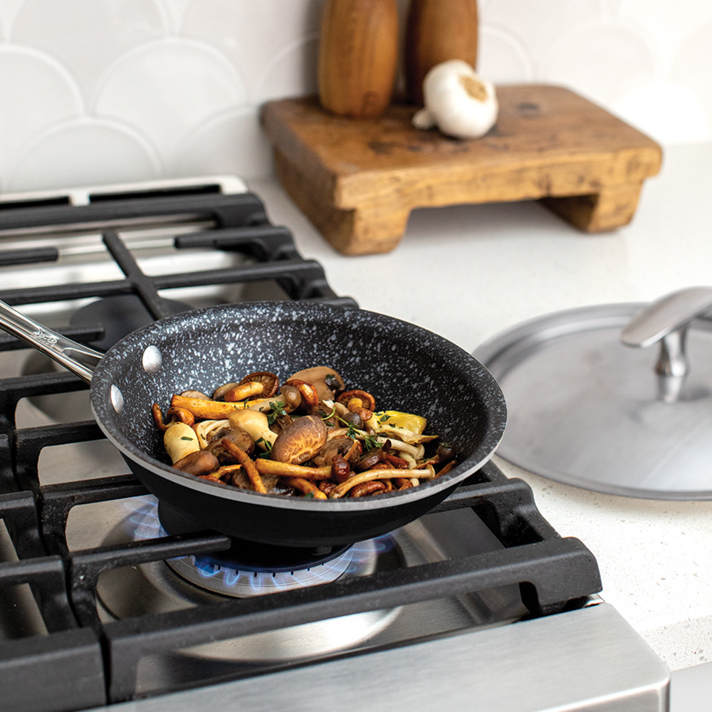 Nordic Ware 8-inch black ceramic skillet with sautéed mushrooms on stovetop, matching lid on counter