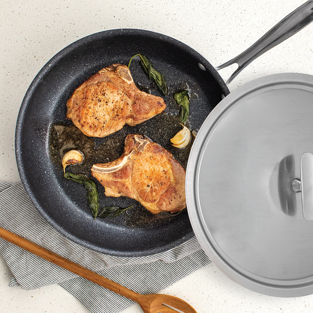 Nordic Ware 12-inch Basalt skillet with fitted lid, containing seared pork chops with golden-brown crust
