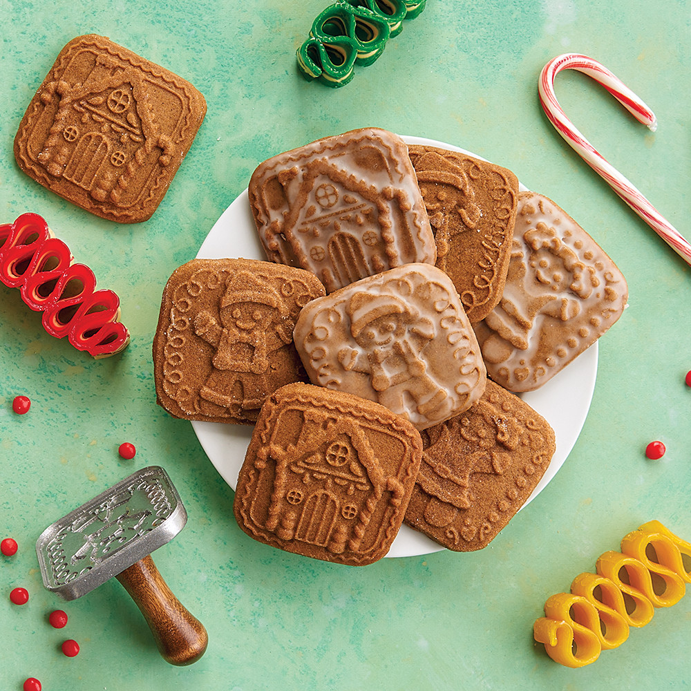 Decorated gingerbread cookies made with Nordic Ware cookie stamps on white plate, surrounded by colorful holiday candies