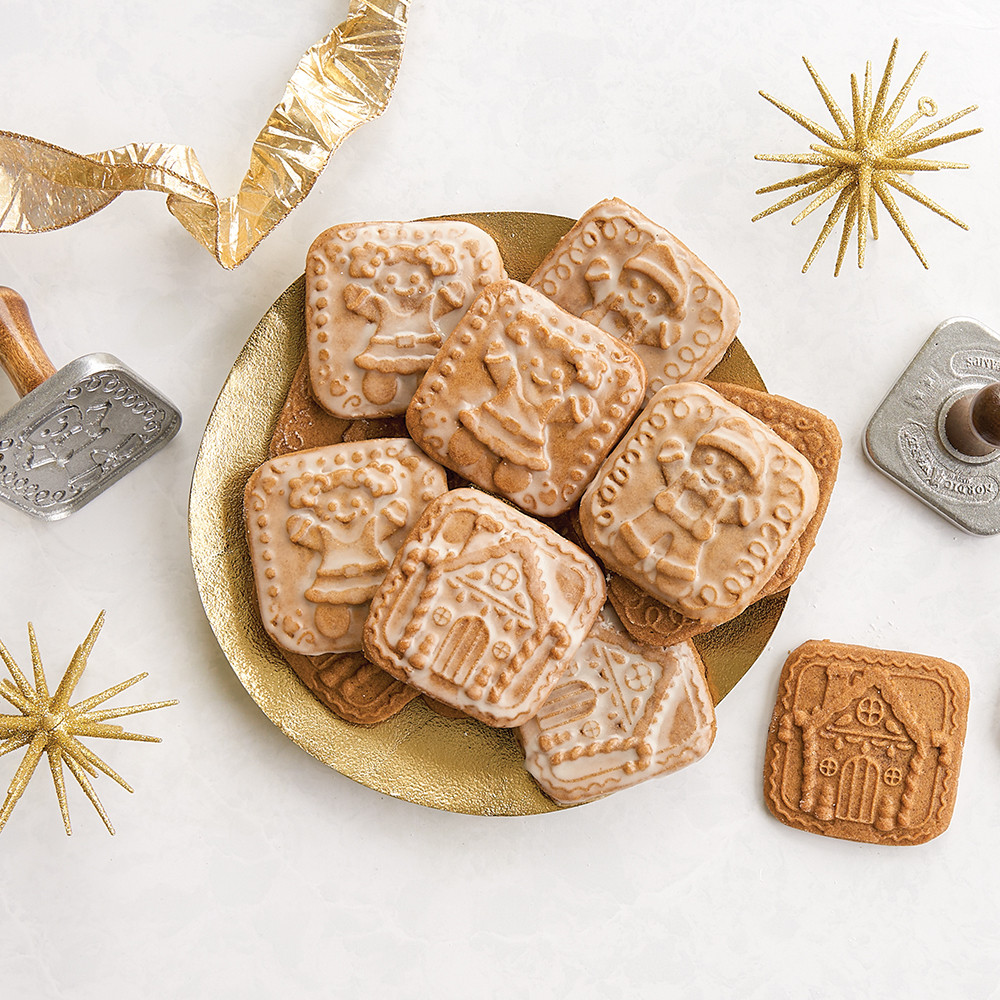 Four glazed gingerbread cookies with Nordic Ware wooden cookie stamps displaying detailed imprinted designs on gold plate