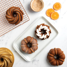 Two golden bundt cakes on white plates next to Nordic Ware aluminum Bundt Duet pan with cooling rack