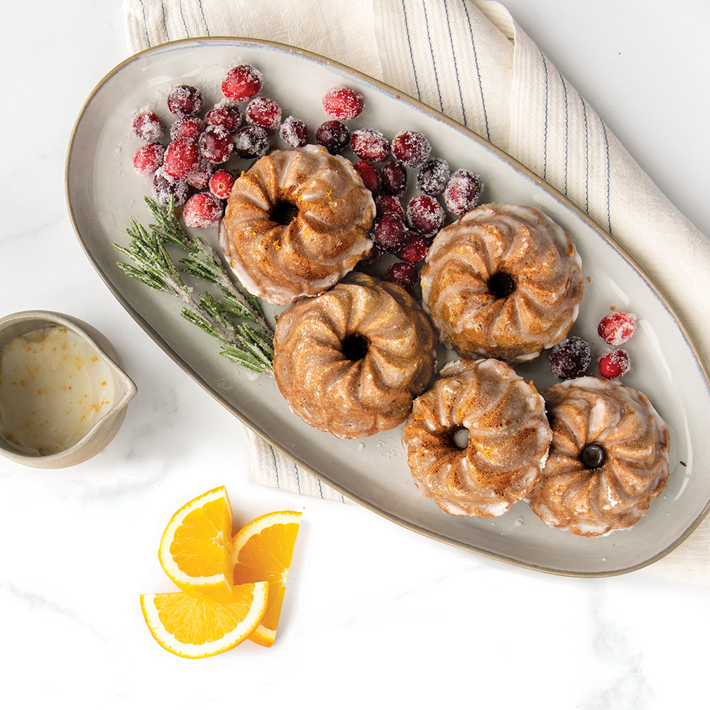 Six golden mini bundt cakes with swirled pirouette design from Nordic Ware aluminum bundtlette pan, garnished with orange slices