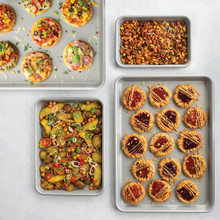 Nordic Ware 4-piece nonstick sheet pan set with baked cookies, roasted vegetables, and golden dinner rolls