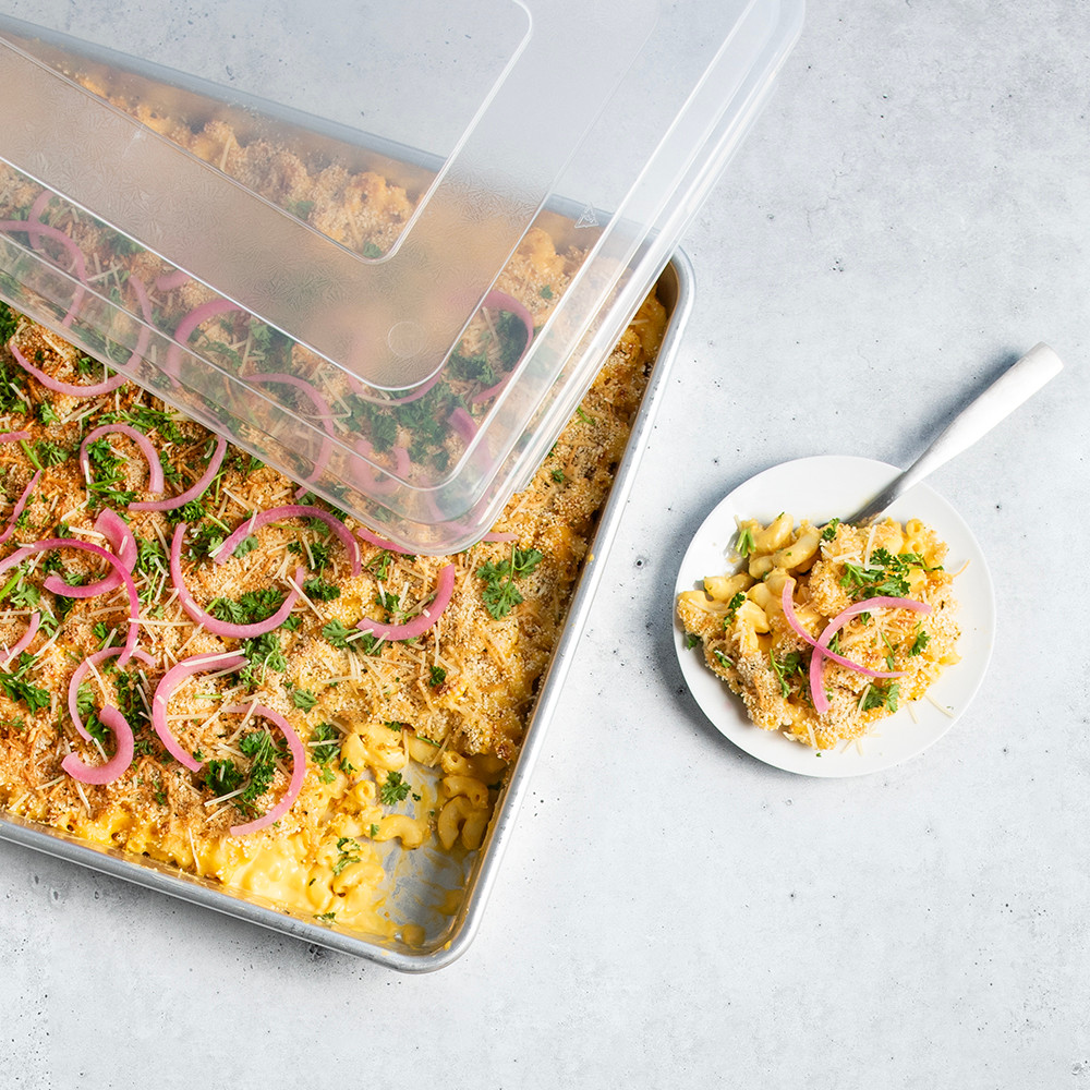 Nordic Ware aluminum Big Batch Pan with lid, containing creamy mac and cheese, plated portion alongside