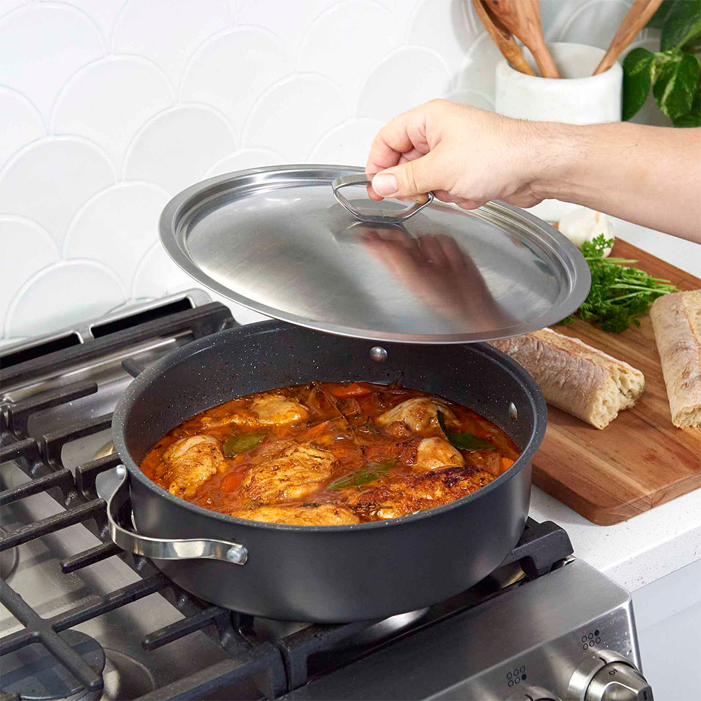 Nordic Ware Verde braiser pan with lid on stovetop, containing simmering chicken and vegetable stew