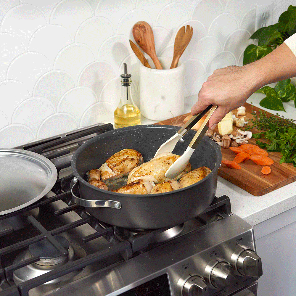 Green Nordic Ware braiser pan cooking chicken with vegetables on stovetop, lid being lifted to show contents