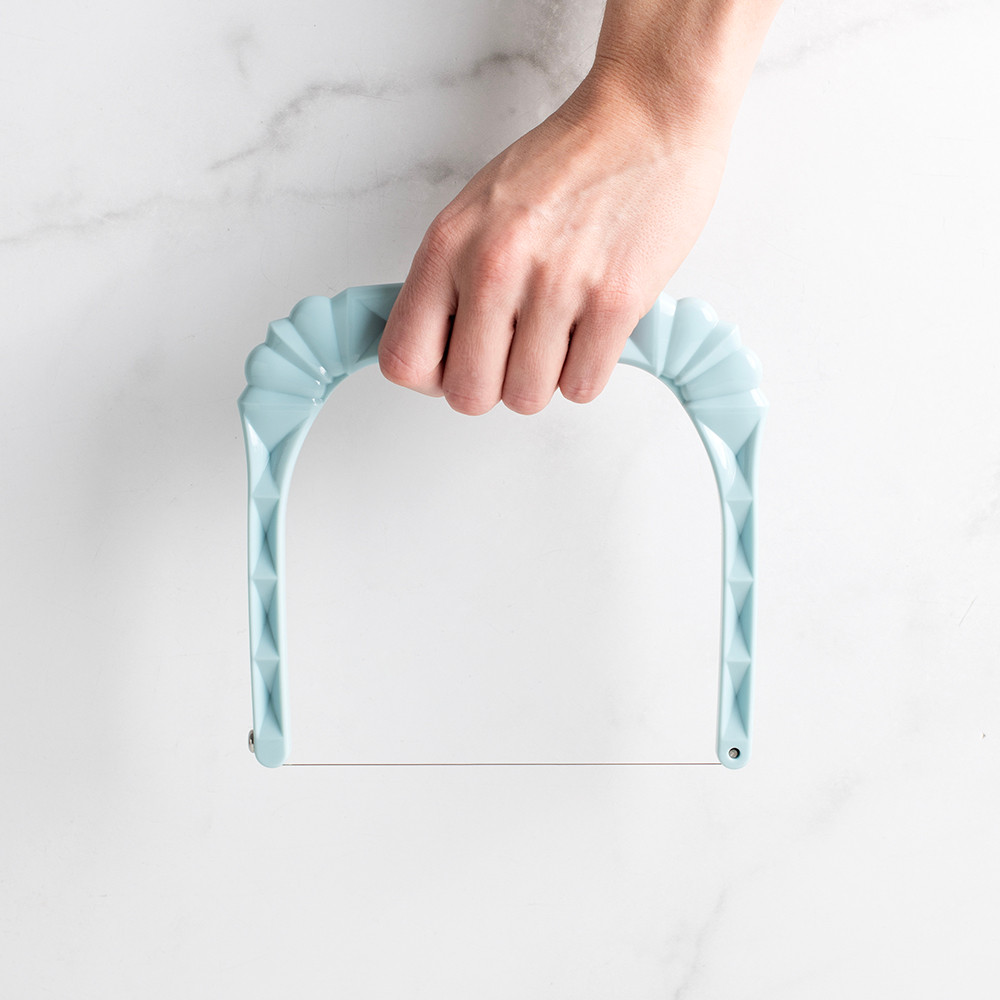 Hand holding Nordic Ware white plastic bundt slicer tool showing size comparison against palm