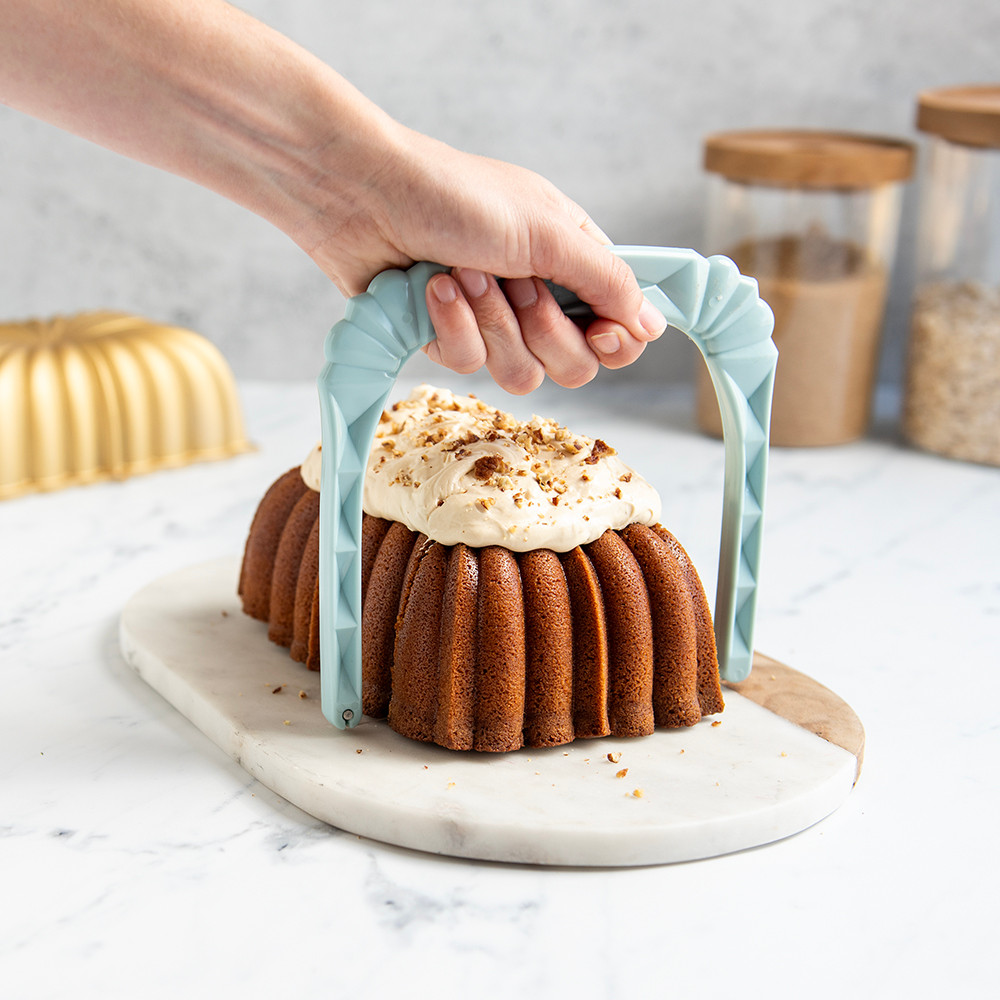 Nordic Ware white plastic bundt slicer cutting golden baked fluted loaf cake into even slices