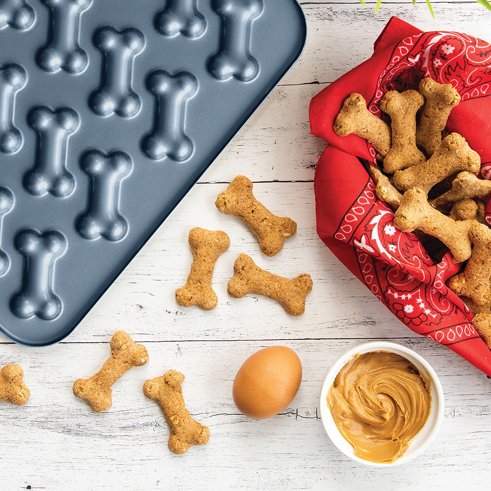 Blue Nordic Ware Puppy Love Treat Pan with golden-brown bone-shaped dog treats arranged beside it
