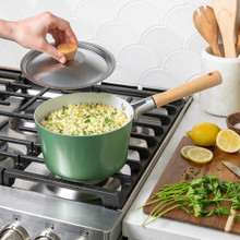 Nordic Ware cardamom-colored 3-quart saucepan with lid on stovetop, filled with cooked rice, hand lifting lid
