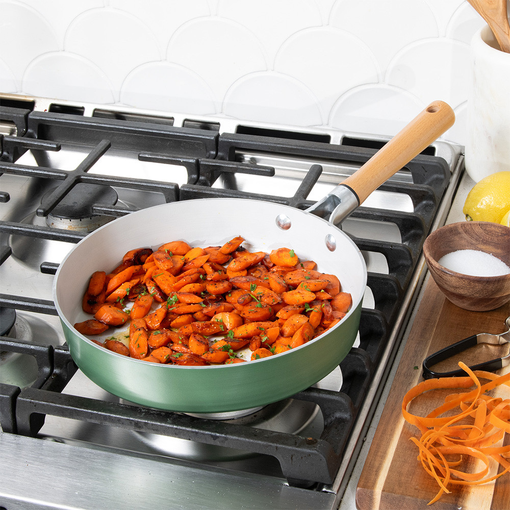 Nordic Ware cardamom ceramic nonstick 10-inch skillet on stovetop with diced carrots cooking inside