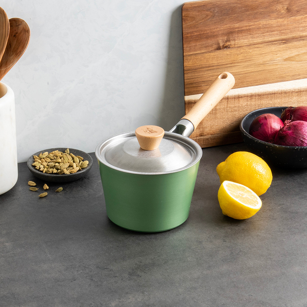 Nordic Ware stainless steel saucepan with cardamom lid on marble counter, surrounded by cooking ingredients and wooden utensils