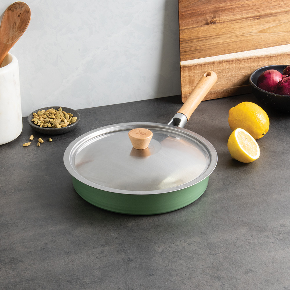 Nordic Ware stainless steel 10-inch sauté pan with matching lid on countertop, surrounded by fresh cooking ingredients