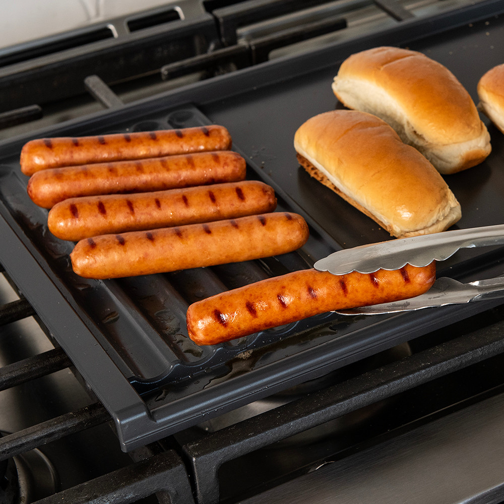 Nordic Ware Basalt dual-zone grill griddle with tongs holding grilled hot dog over ribbed surface