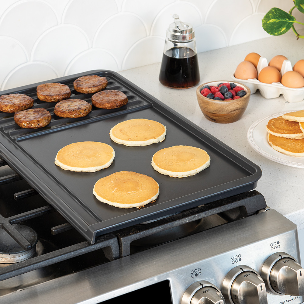 Nordic Ware black basalt dual-zone grill griddle on stovetop with golden pancakes and browned sausage patties