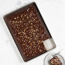 Nordic Ware Prism aluminum big batch pan with lid, rectangular, containing chocolate cake with one square piece cut and served on white plate