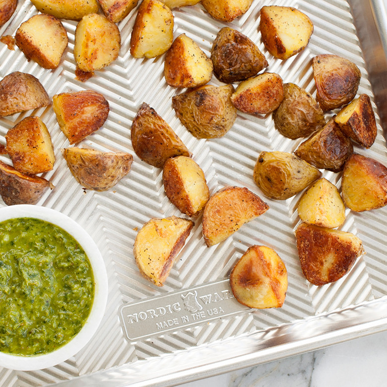 Golden roasted baby potatoes with herbs and dipping sauce on Nordic Ware aluminum Prism half sheet pan