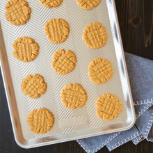 Golden brown peanut butter cookies arranged on Nordic Ware Prism aluminum half sheet pan with textured surface