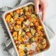 Hand holding Nordic Ware aluminum Prism eighth sheet pan with colorful roasted vegetables using kitchen towel
