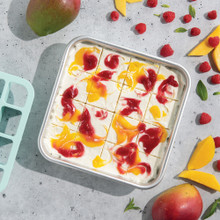 Nordic Ware brownie cutter tool beside square pan of sliced fruit swirl brownies with fresh berries