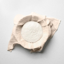 Raw sourdough dough ball wrapped in cream-colored linen towel, nestled inside Nordic Ware aluminum bread pan