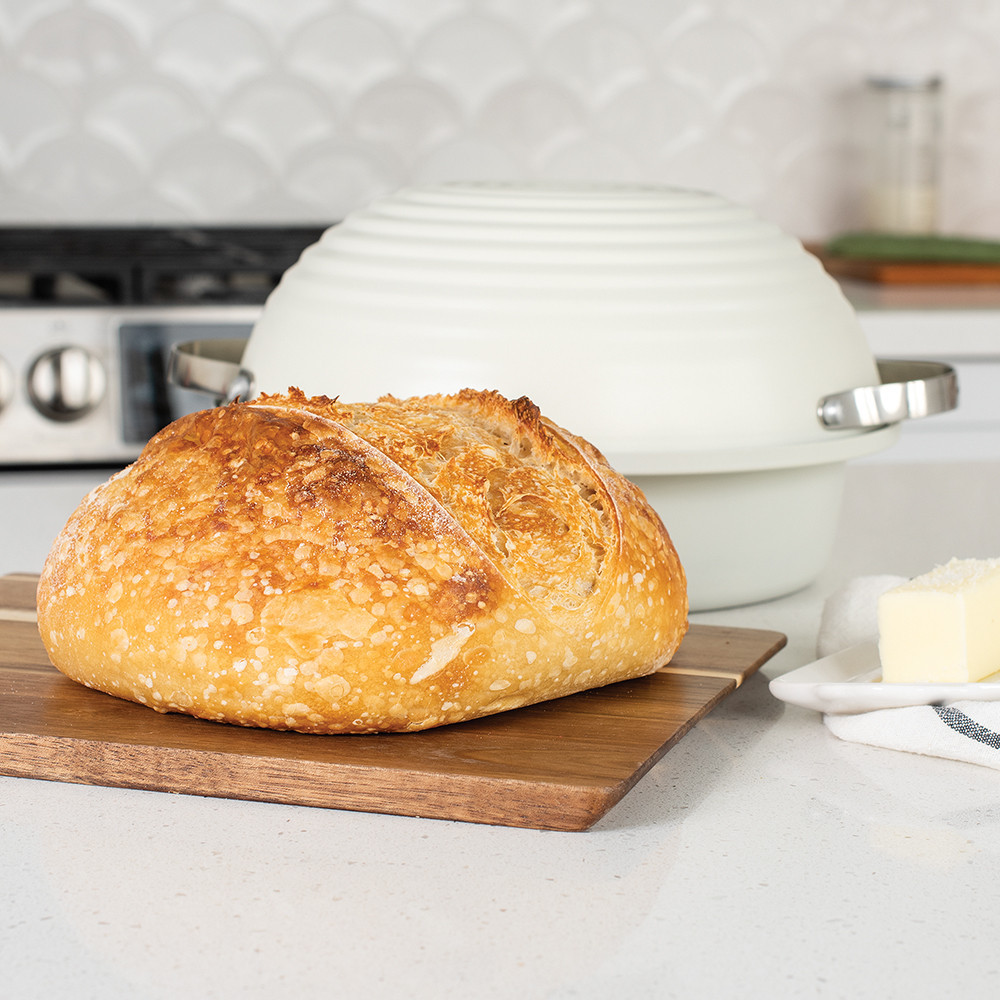 Nordic Ware Simply Sourdough bread baking kit with golden loaf, aluminum pan with lid, and butter on wooden cutting board