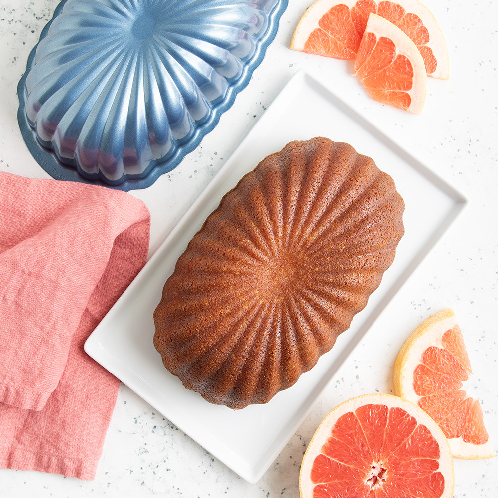 Sliced vanilla pound cake on white plate with Nordic Ware aluminum fluted loaf pan and orange garnish