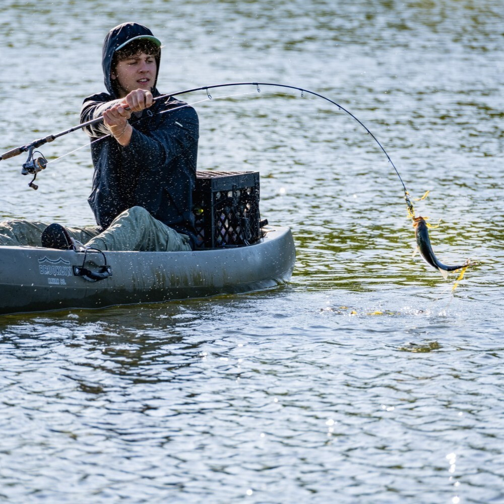 Kayak angler landing a fish with a PaddleOn crate secured behind the seat.