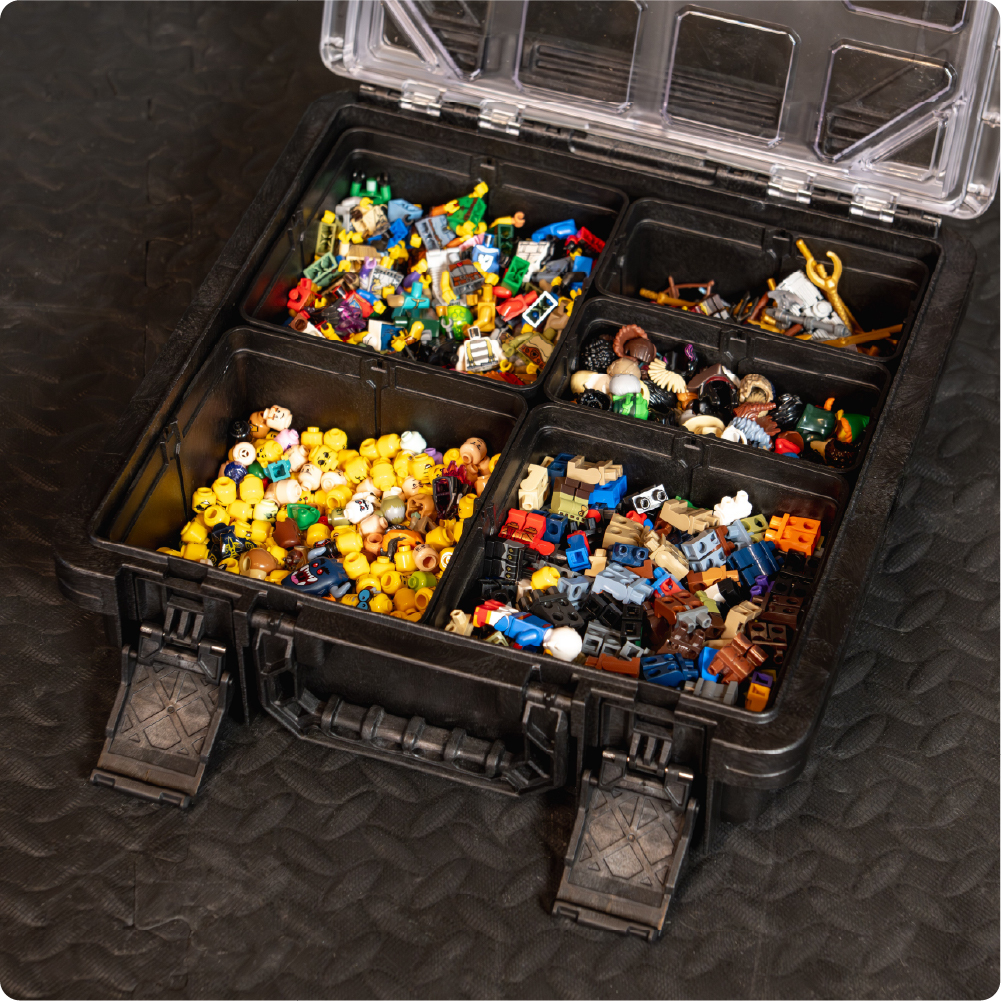 Open black BaseBox with divided compartments organizing LEGO-compatible minifigure parts, accessories, and small building pieces.