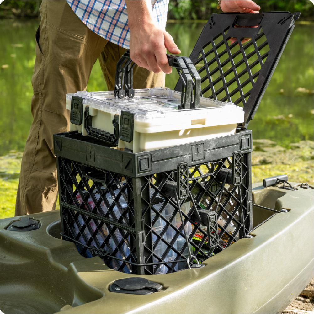 Person lifting a clear-lid BaseBox from a black UbeCube crate mounted on a kayak.