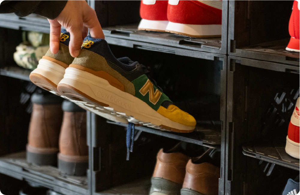 Hand placing a sneaker into a black UbeCube UC02 Lidless crate shoe storage setup with shelf kits dividing each crate into stacked shoe compartments.
