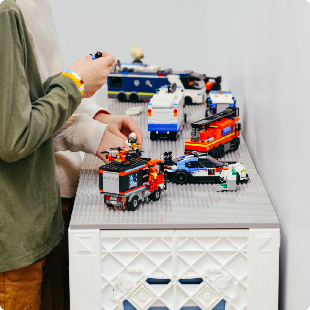 Children playing with LEGO vehicles on a gray CratePlay build plate mounted on white UbeCube crates.
