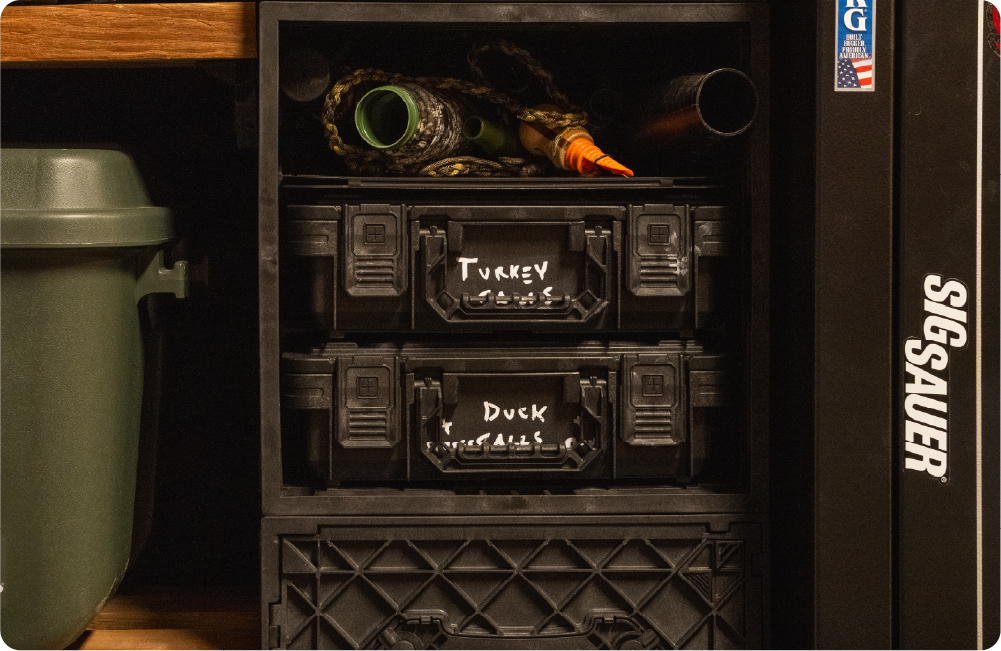 Black UbeCube storage setup with two labeled BaseBoxes for turkey and duck gear, stored with hunting calls and equipment on a shelf.