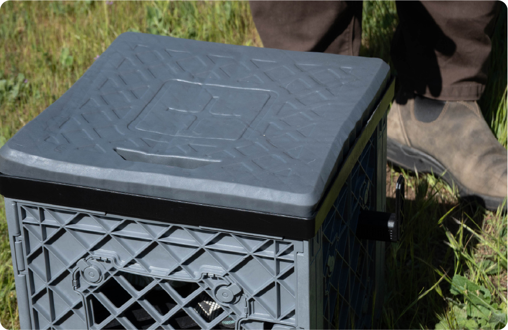 Gray UbeCube crate with a black lid being used as a seat or storage box outdoors near the water.