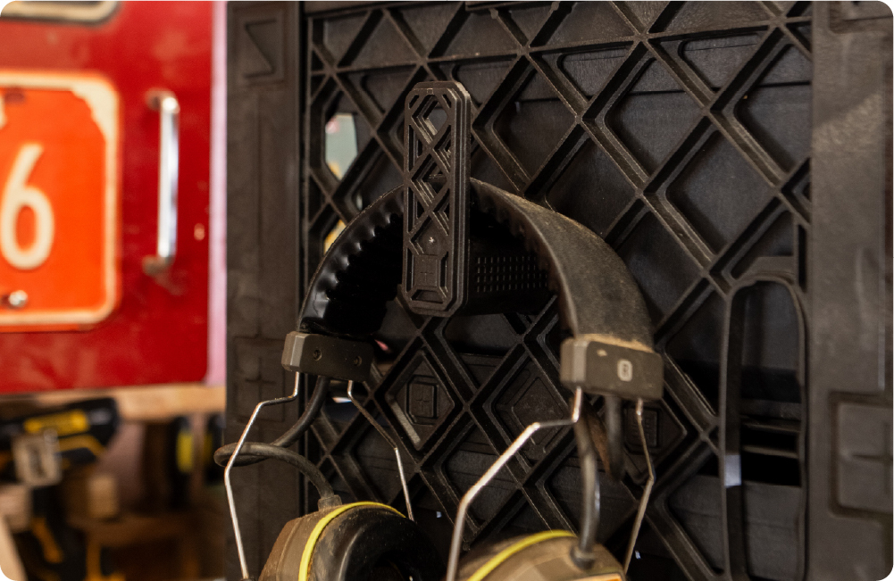 Black UbeCube crate with ear protection hanging from a side-mounted CrateHook in a workshop setup.
