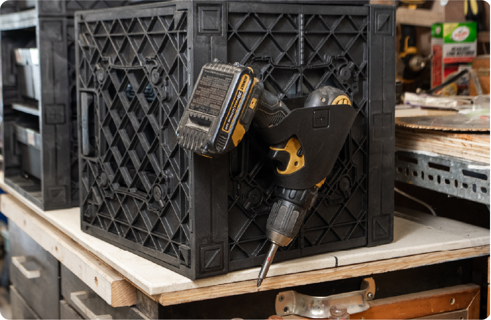 Black UbeCube crate with a cordless drill stored in a side-mounted Drill Holder on a workbench.