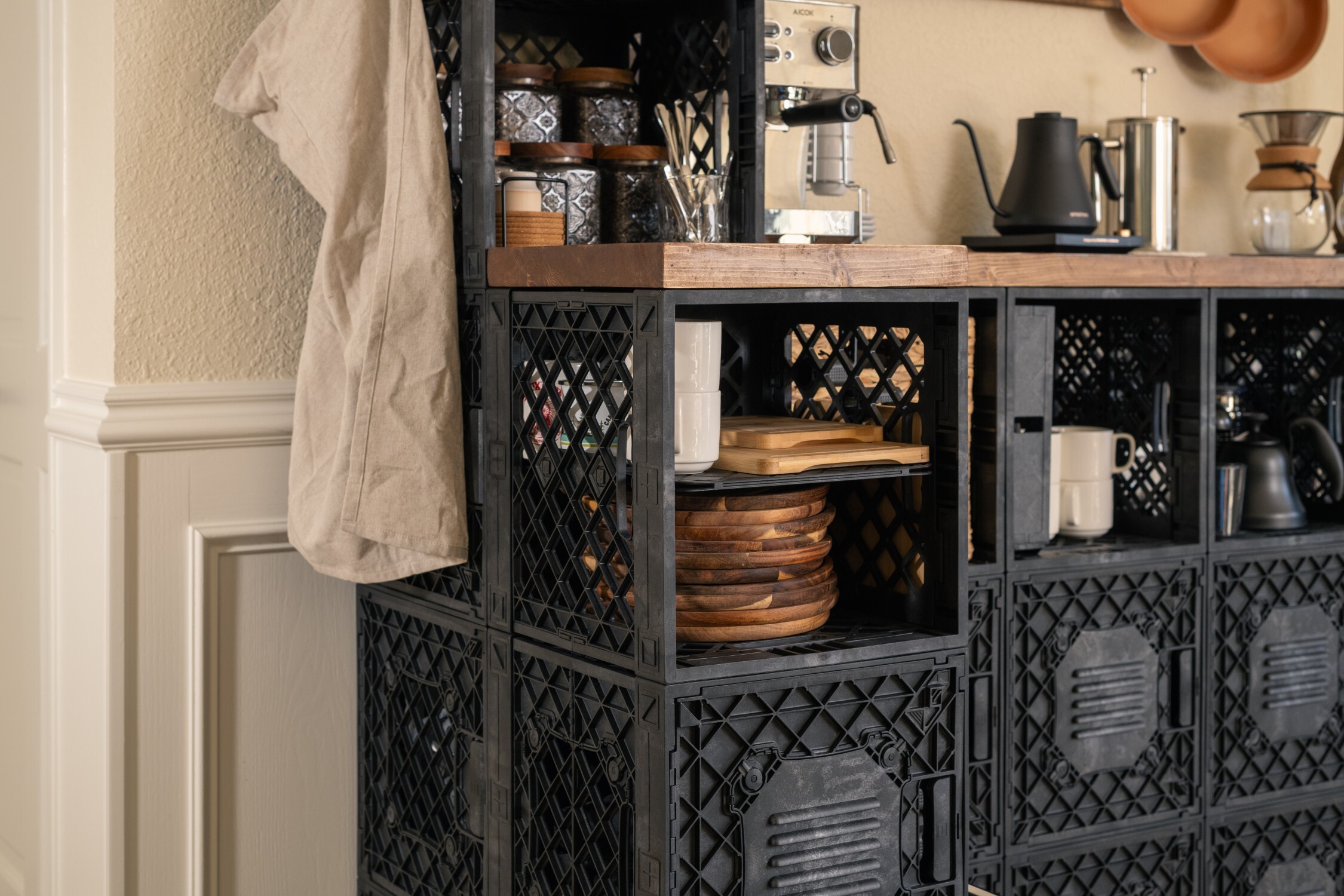 Coffee station side view with towel, mugs, and appliances stored in crates.