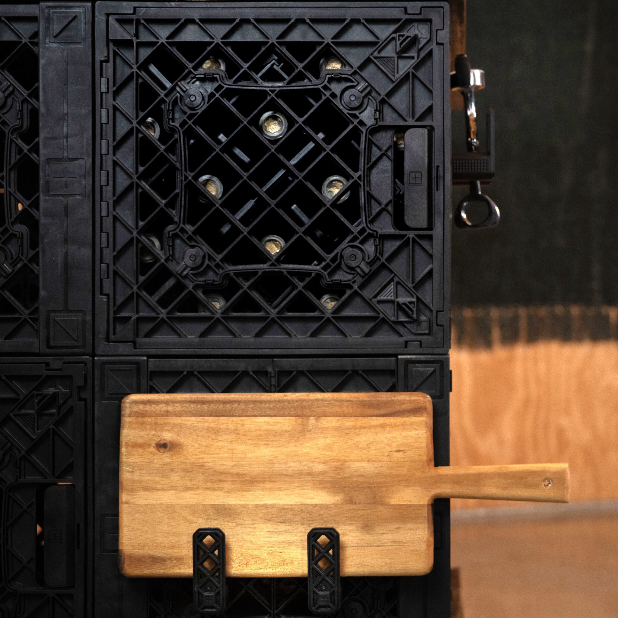 Close-up of wine bottles behind crate grate with cutting board and tools.