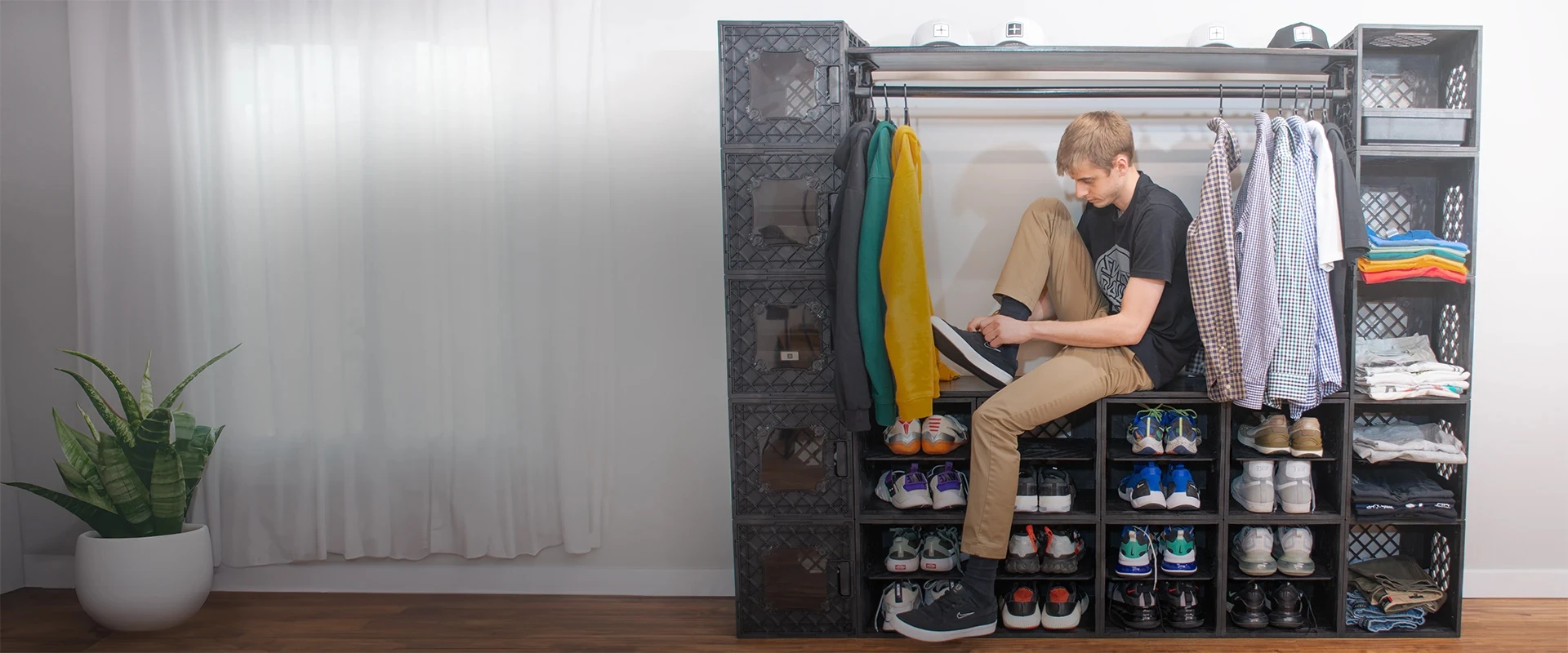 Man tying shoes in front of a modular CrateCloset™ setup with hanging clothes, folded shirts, and organized sneakers.