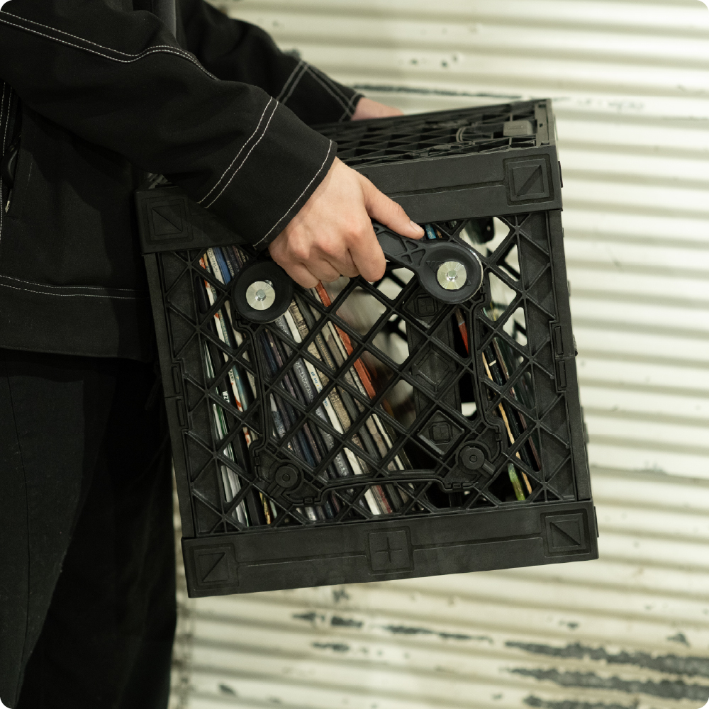 Person carrying a black UbeCube CrateVinyl filled with records using the side-mounted Handle Kit.