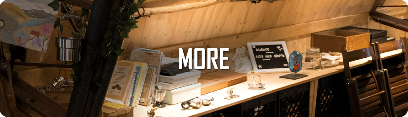 Creative workspace with UbeCube crates used for storage under a wooden workbench, surrounded by books, art supplies, and decor items, labeled ‘MORE’.