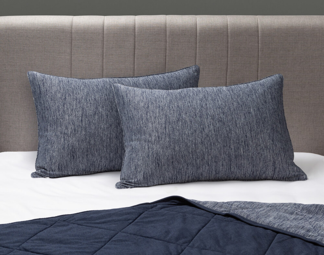 Nos taies d'oreiller Cool Touch en bleu marine sont posées sur un lit blanc et gris avec une couverture assortie en dessous.
