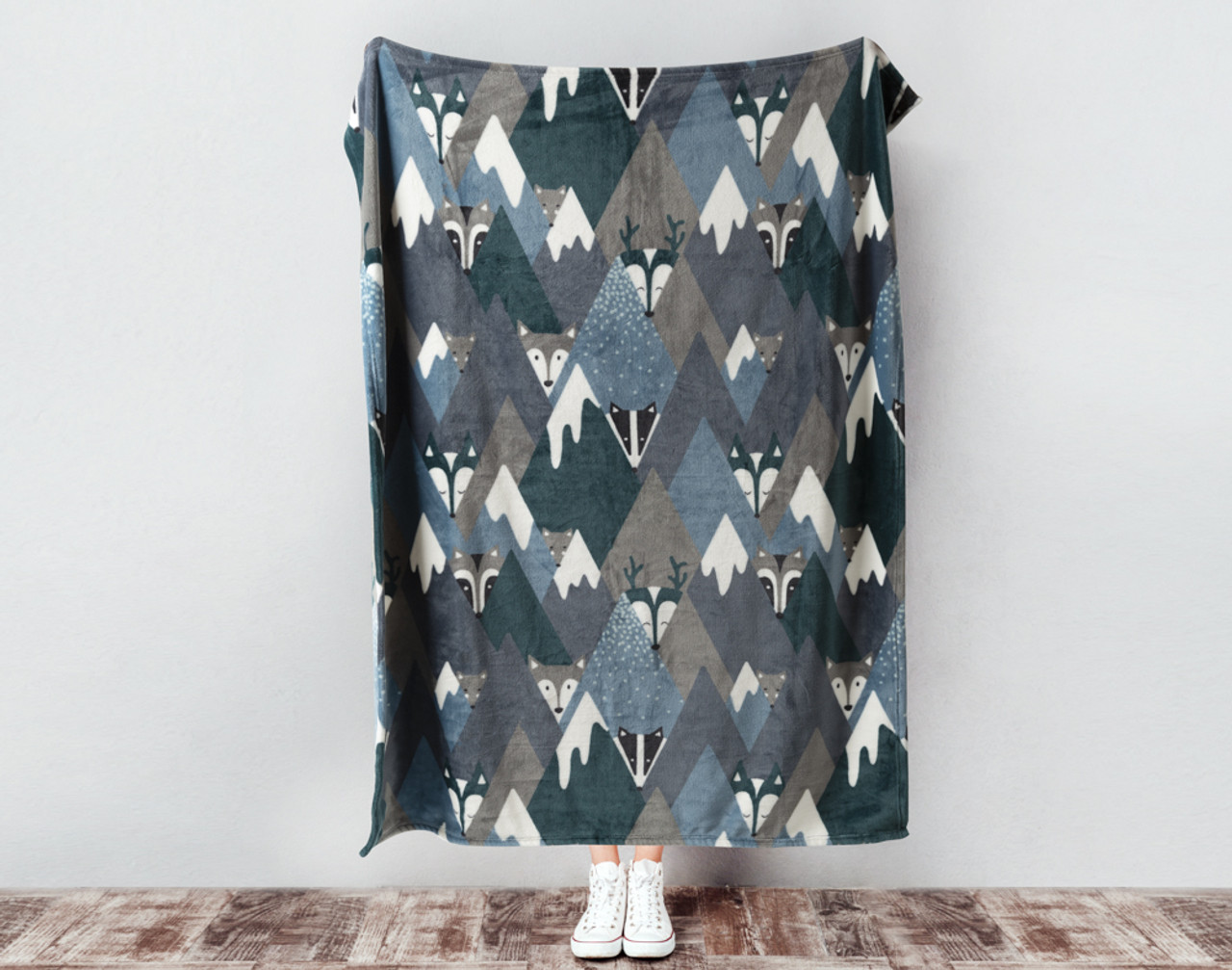 Our Kid's Fleece Velveteen Throw in Mountain Animals being held against a wall with triangular critter faces and a diamond mountain pattern.