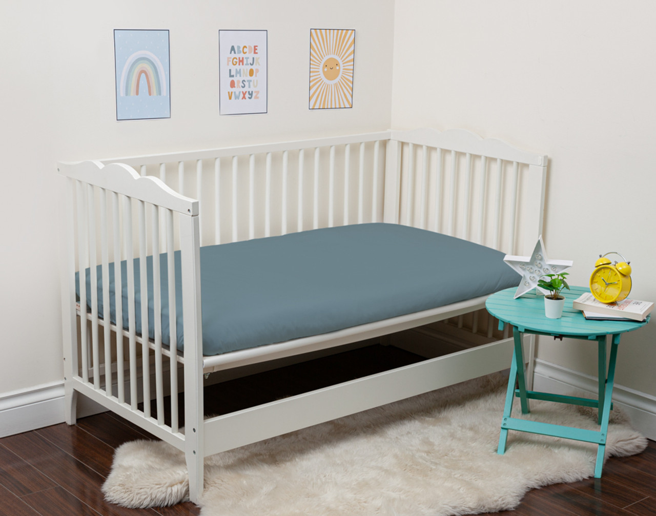 Notre Bamboo Cotton Crib-Sized Fitted drap in Spruce s'habille sur un petit matelas dans un lit d'enfant ouvert.